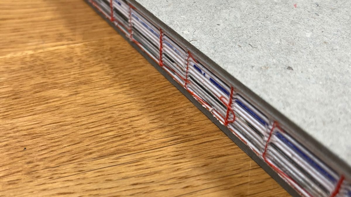 Offener Rücken der Steifbroschur mit orangefarbenem Heftfaden im Detail