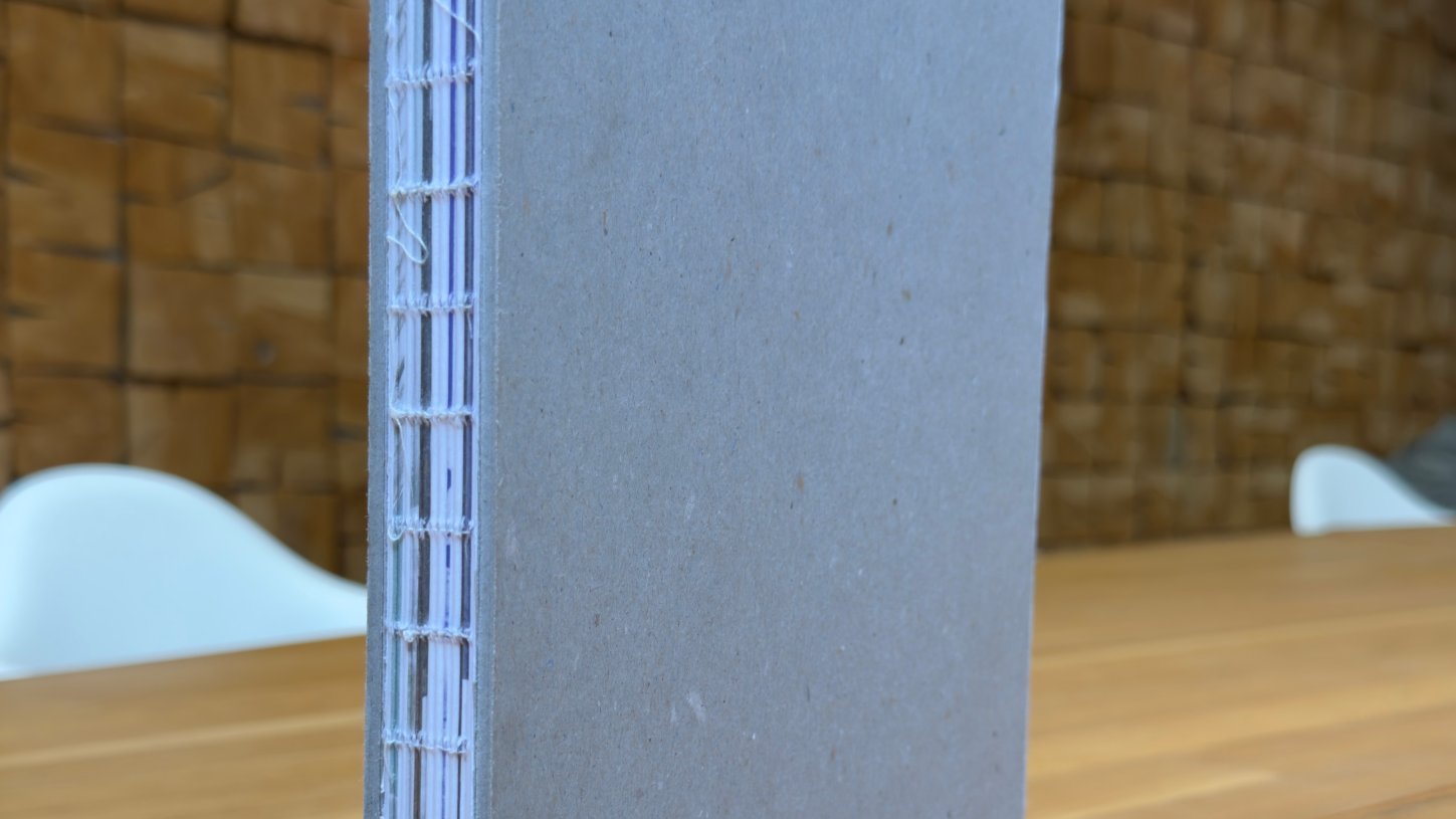 Offene Fadenheftung: Buch mit Graupappe-Umschlägen und naturweißem Heftfaden am offenen Rücken