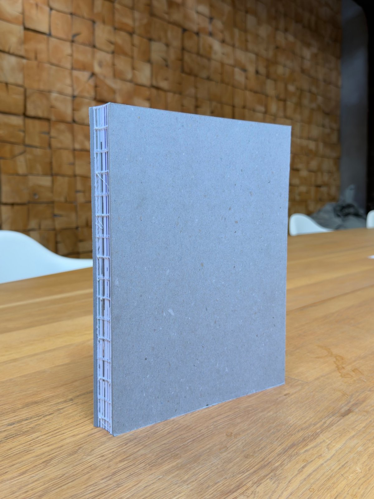 Stehendes Buch mit offener Fadenheftung: Graupappe-Umschläge und sichtbare Lagen am offenen Rücken